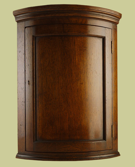Hanging corner cupboard, Georgian style, in English oak, with curved front frame and door.