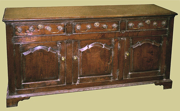 3 drawer dresser base in oak, with shaped fielded panel cupboard doors, cockbeaded drawers, bracketed feet and solid brassware.