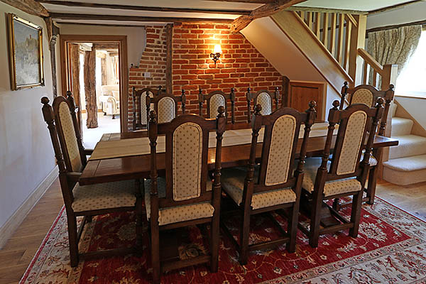 Oak pedestal dining table, upholstered side chairs and armchairs, in dining room of Kent country cottage