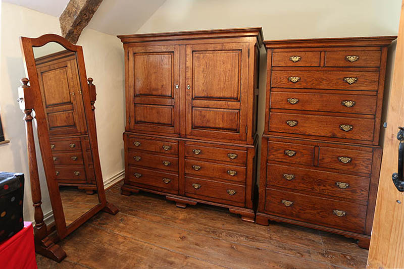 Oak linen press, chest on chest and cheval mirror, in bedroom of old cottage