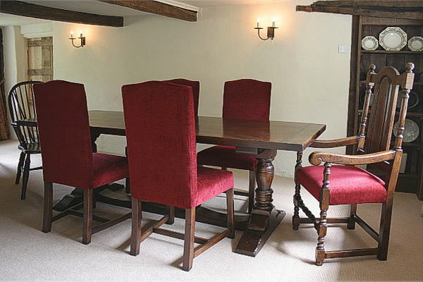 Oak pedestal dining table and upholstered side chairs and armchair, in Sussex thatched cottage.