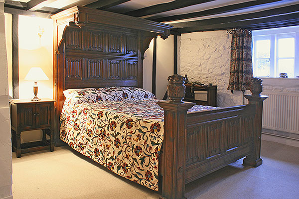 Handmade linenfold panelled oak half tester bed, in beamed bedroom of timber framed cottage.