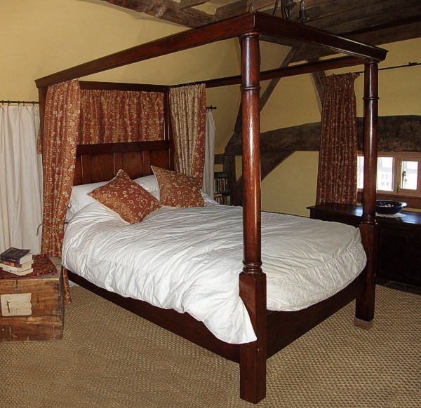 18th century style oak four poster bed, in heavily beamed bedroom of timber framed house.