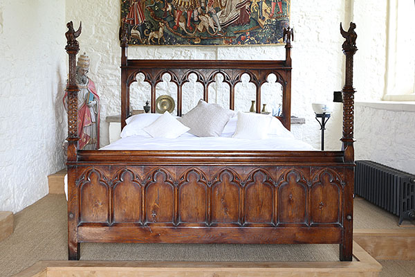 Gothic style carved oak bed on raised dais in Sussex manor house converted chapel.