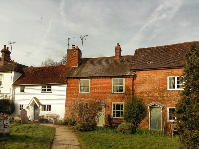 Brick and weather boarded cottages line the church path in Cowfold