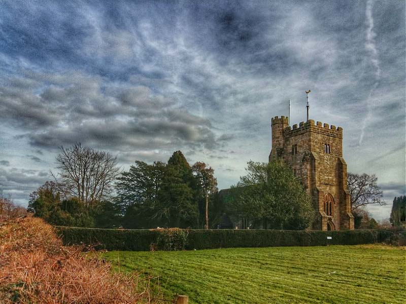 The 15th century west tower of Cowfold church, viewed from the village recreation field towards the end of church path