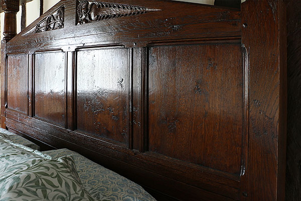 Carved oak headboard on bespoke Tudor style pencil bed.